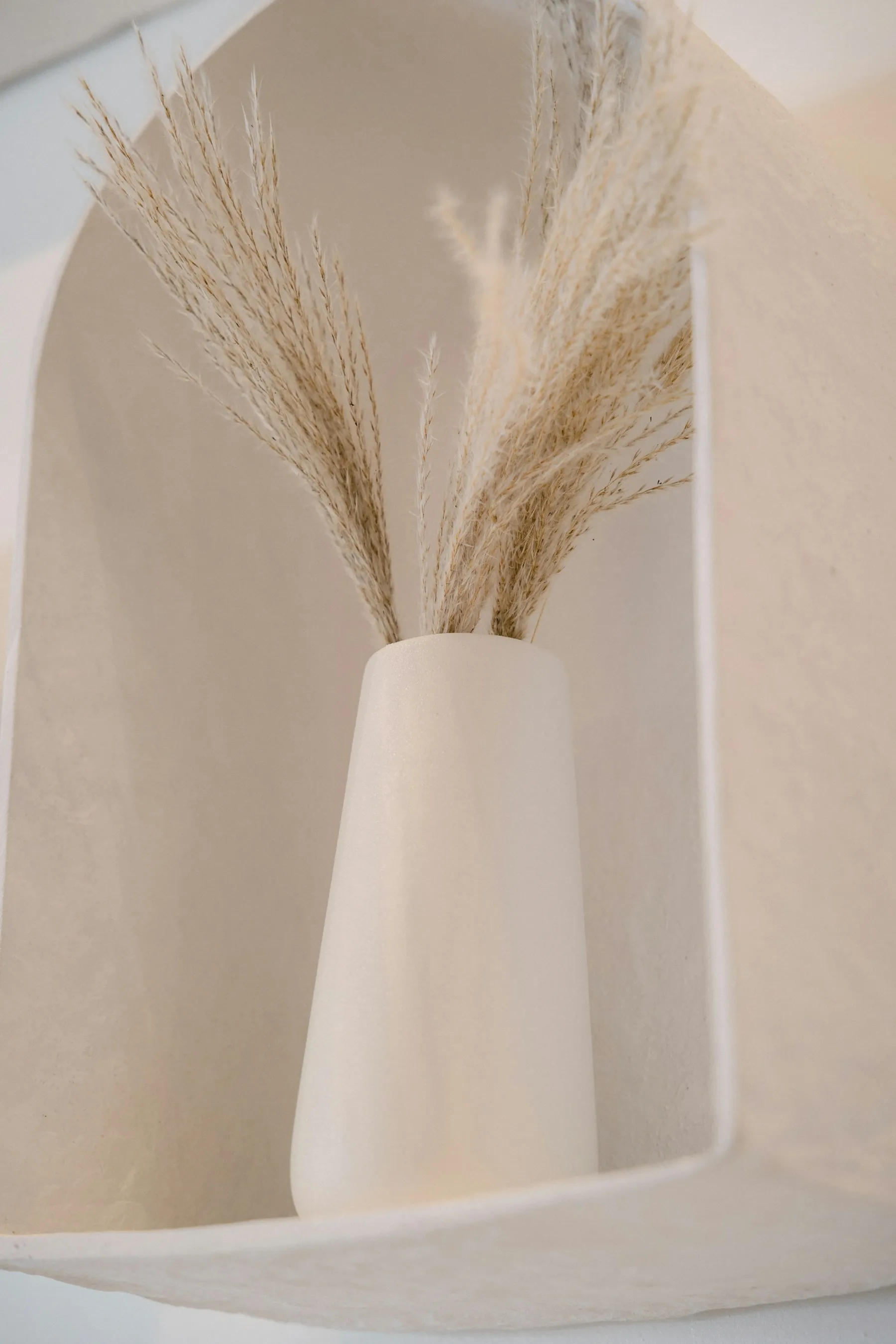 A white ceramic vase holding dried grasses on a quiet shelf
